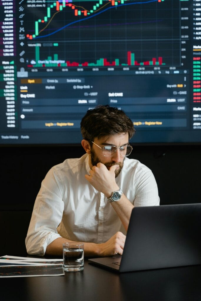 Current image: Pensive businessman with a beard analyzing stock market trends on a laptop in an office setting.
