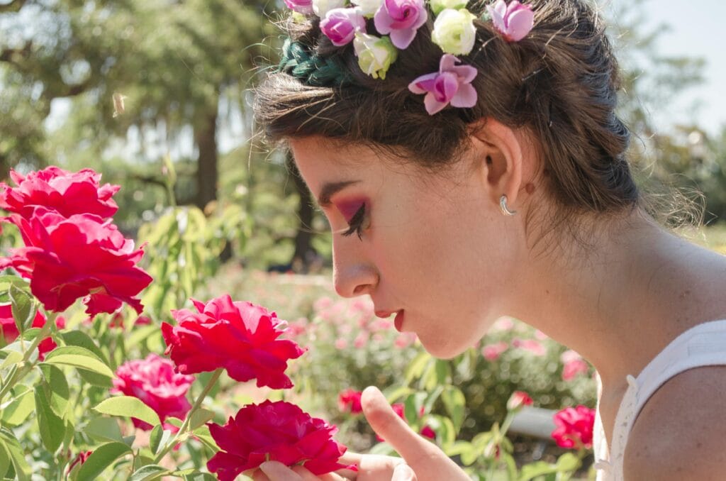 Current image: A woman with a floral crown enjoys the fragrant roses in a sunny garden setting.