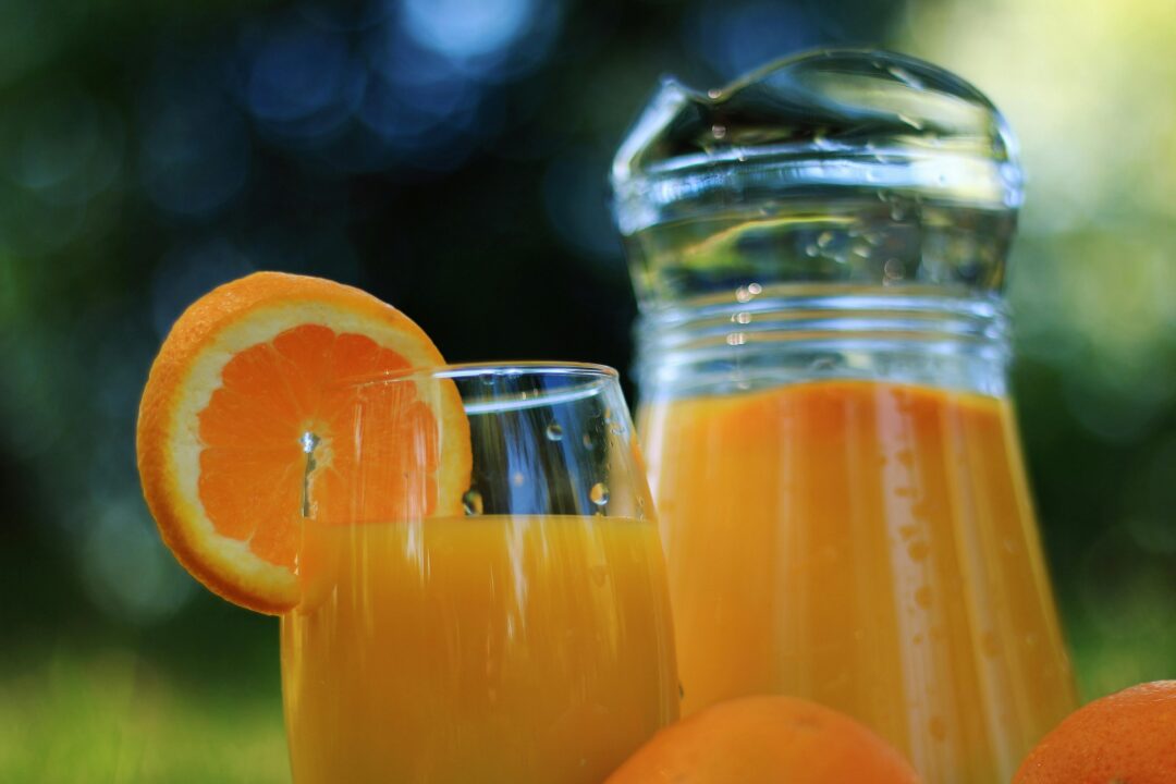 Current image: Close-up of a refreshing glass of orange juice with fresh oranges outdoors.