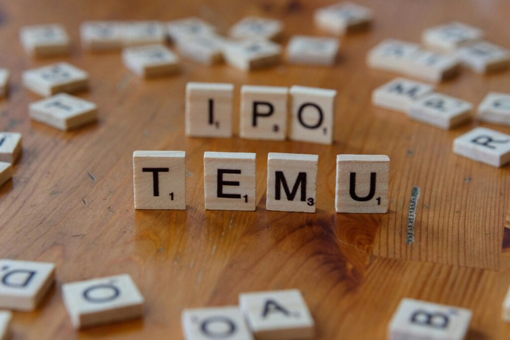 Current image: Scrabble tiles spelling IPO and Temu placed on a wooden table surface.